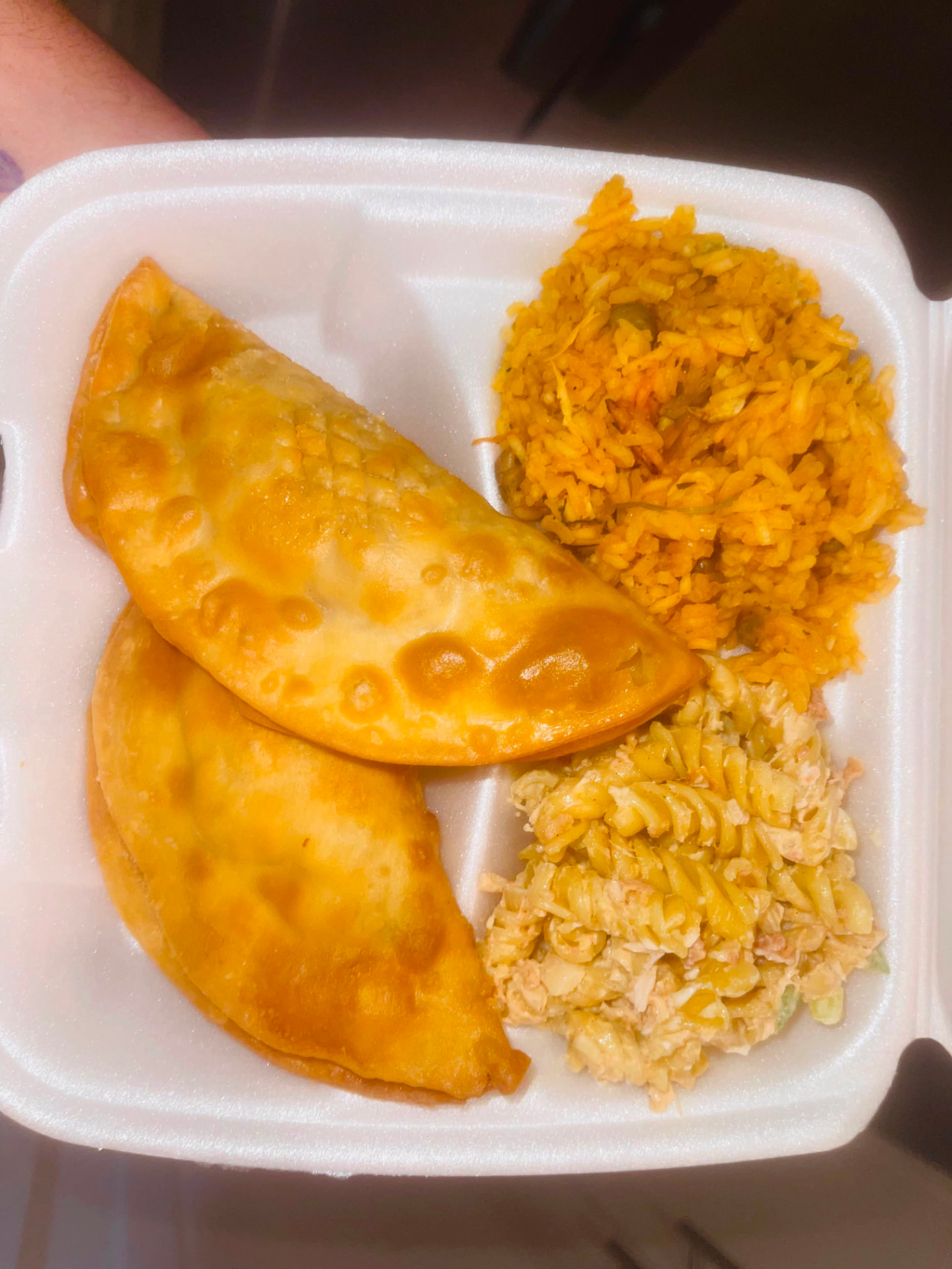 Two golden empanadas with arroz con gandules and antipasta salad in a takeout tray
